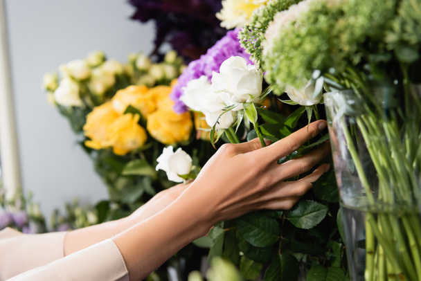 Przycięty widok kobiety kwiaciarnia troszcząc się o białe róże na stojaku kwiatów w sklepie na rozmytym tle - Zdjęcie, obraz