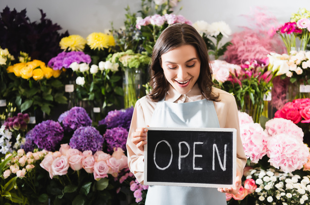 Excited florist looking at chalkboard with open lettering near range of flowers on background - Photo, Image