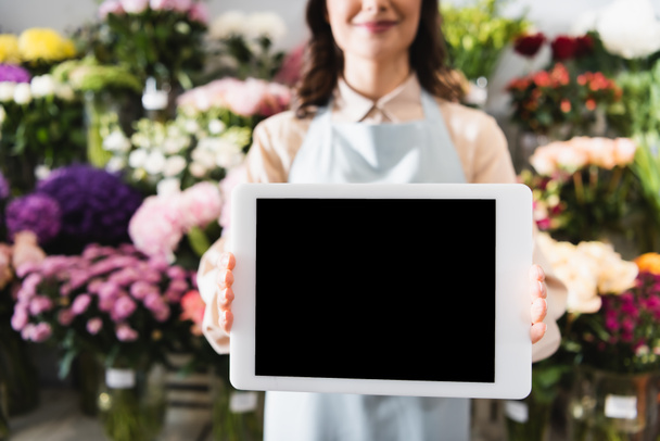 Ausgeschnittene Ansicht der Blumenhändlerin zeigt digitale Tablette mit leerem Bildschirm mit verschwommenem Bereich von Blumen auf dem Hintergrund - Foto, Bild