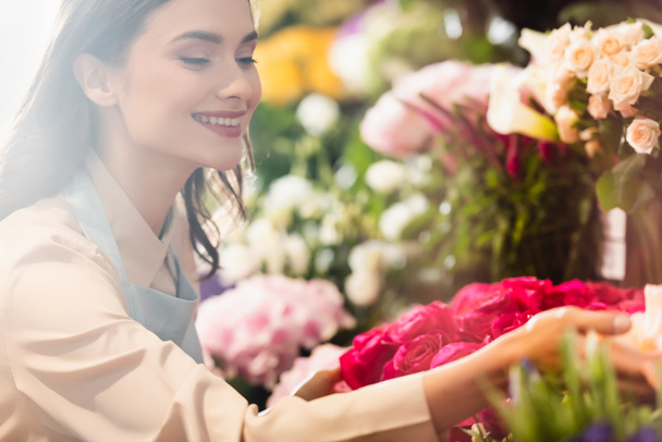 Szczęśliwy kobieta kwiaciarnia opiekuńczy o kwiaty na zamazanym tle - Zdjęcie, obraz