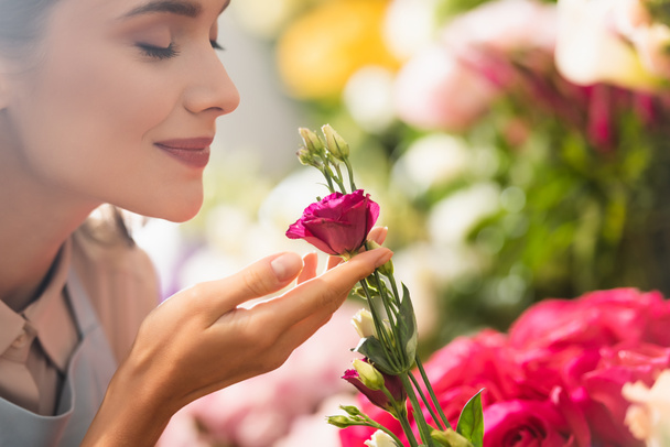 Szczęśliwy kobieta kwiaciarnia z zamkniętymi oczami pachnący kwiat eustoma z niewyraźne kwiaty na tle - Zdjęcie, obraz