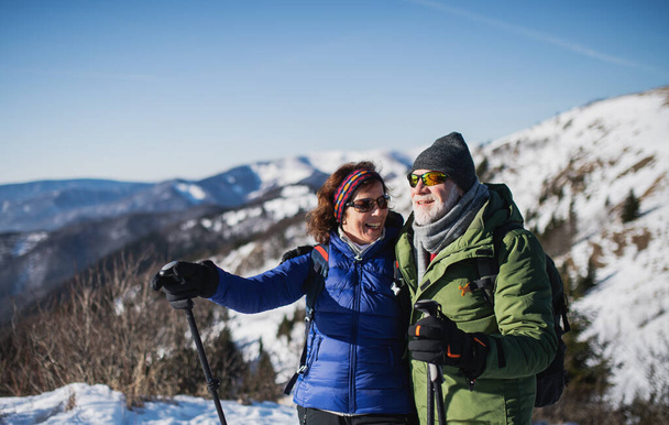 Senior couple hikers with nordic walking poles in snow-covered winter nature. - Foto, Imagem