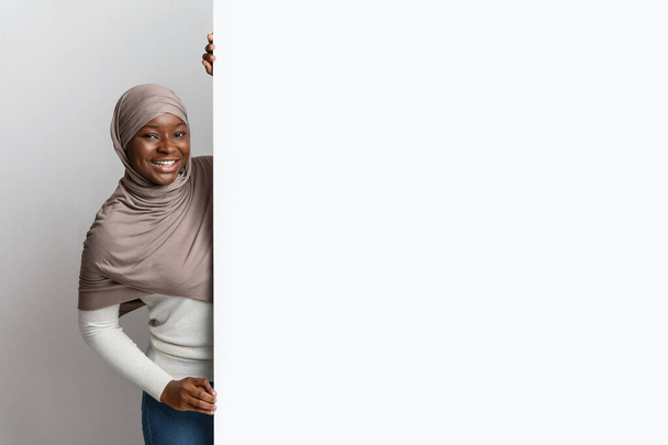 Tesettürlü neşeli siyah Müslüman kadın elinde büyük beyaz reklam panosu tutuyor. - Fotoğraf, Görsel