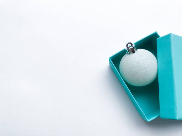 Τυρκουάζ κουτί κόσμημα μέσα του οποίου είναι μια λαμπερή λευκή μπάλα Χριστουγέννων. Λευκό φόντο. Αντιγραφή χώρου. - Φωτογραφία, εικόνα