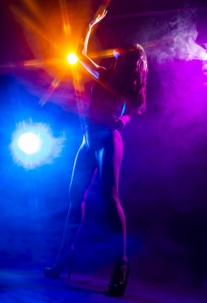 Beautiful slim sexy dancer girl wearing lingerie and high heels posing in the rays of light in a colorful smoke. Artistic, conceptual, silhouette,commercial and advertising design. - Фото, зображення