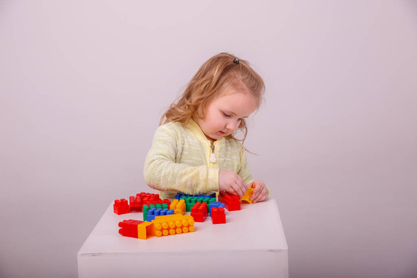 pequeña linda chica rubia jugando en un constructor sobre un fondo blanco. Concepto de educación preescolar - Foto, imagen
