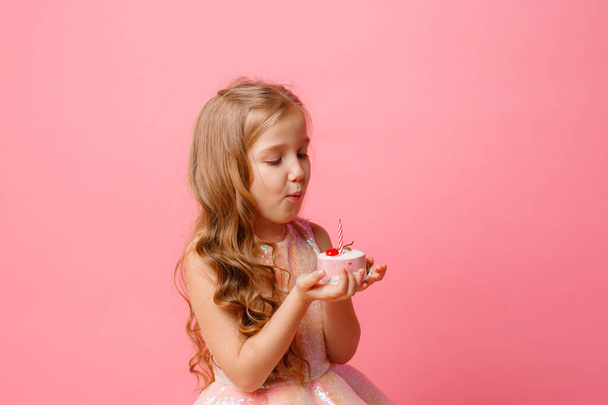 χαριτωμένο κοριτσάκι ποζάρουν σε ροζ φόντο με cupcake γενεθλίων - Φωτογραφία, εικόνα