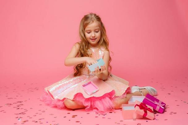 una niña pequeña sosteniendo un regalo en sus manos sonríe sobre un fondo rosa.  - Foto, Imagen