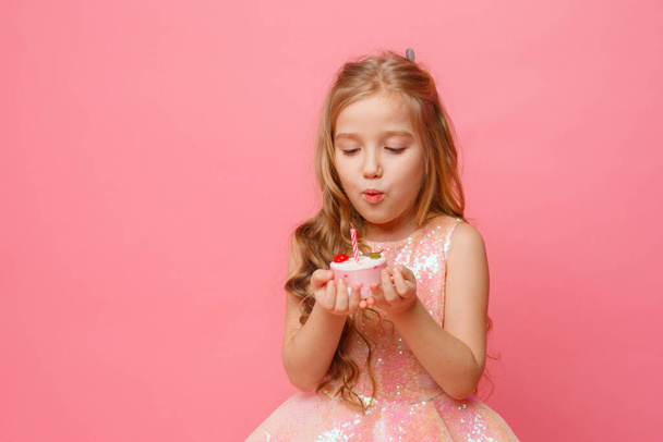 χαριτωμένο κοριτσάκι ποζάρουν σε ροζ φόντο με cupcake γενεθλίων - Φωτογραφία, εικόνα