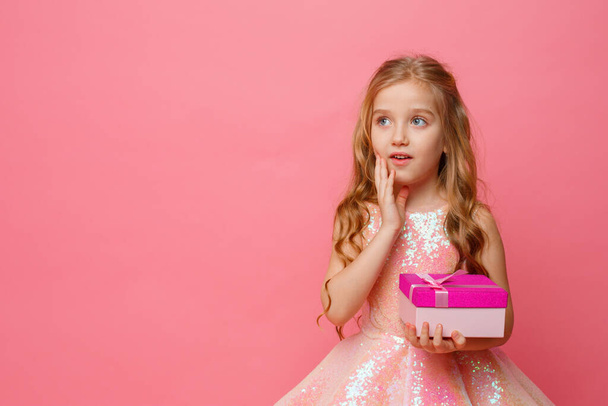 mała dziewczynka trzymająca prezent w dłoniach uśmiecha się na różowym tle. - Zdjęcie, obraz