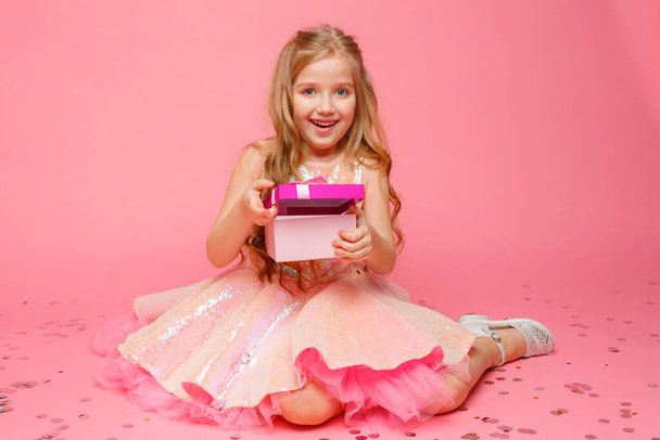 Elinde hediye tutan küçük bir kız pembe bir arka planda gülümsüyor..  - Fotoğraf, Görsel