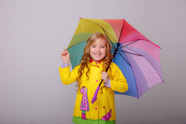 χαριτωμένο κοριτσάκι ποζάρουν στο στούντιο σε κίτρινο αδιάβροχο με ομπρέλα ουράνιο τόξο  - Φωτογραφία, εικόνα