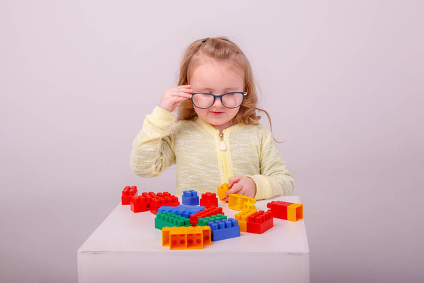 pequeña linda chica rubia jugando en un constructor sobre un fondo blanco. Concepto de educación preescolar - Foto, imagen