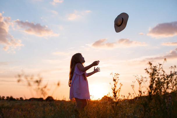 kleines Mädchen mit Hut posiert bei Sonnenuntergang auf einem Feld - Foto, Bild