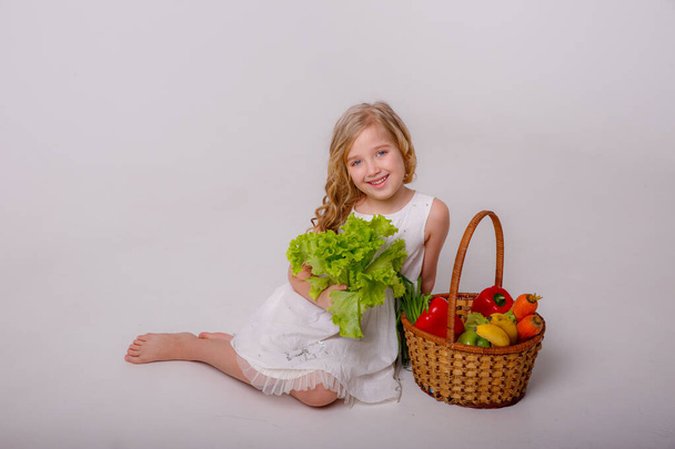 портрет маленькой девочки с корзиной овощей, позирующей в студии - Фото, изображение