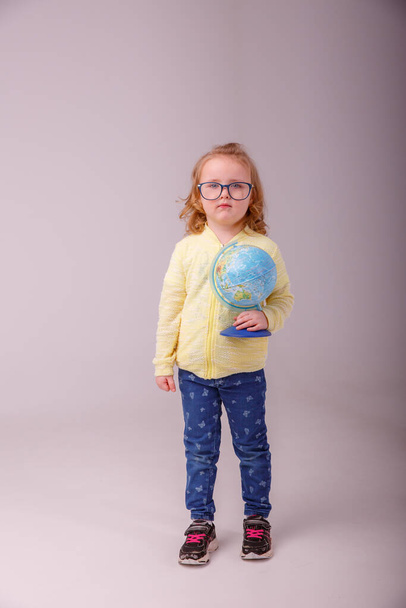 Kis iskolás lány szőke szemüveges egy földgömbbel a kezében mutatja érzelmek boldogság, meglepetés, gondolat, jött fel elszigetelt szürke háttér - Fotó, kép