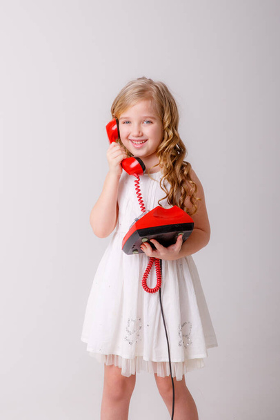 retrato de una niña rubia con un teléfono viejo en sus manos sobre un fondo blanco - Foto, Imagen