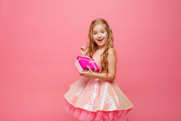een klein meisje met een geschenk in haar handen glimlacht op een roze achtergrond. - Foto, afbeelding