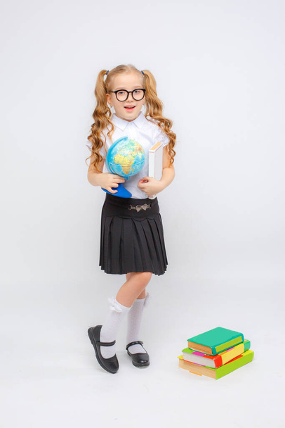 una bambina in uniforme scolastica e occhiali tiene un globo tra le mani su uno sfondo bianco - Foto, immagini