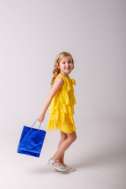 little girl wearing yellow dress and holding shopping bag posing in studio - Foto, imagen