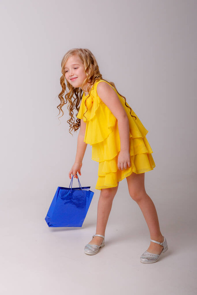 menina vestindo vestido amarelo e segurando saco de compras posando em estúdio - Foto, Imagem