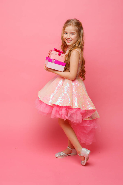 egy kislány kezében egy ajándék mosolyog rózsaszín háttér. - Fotó, kép
