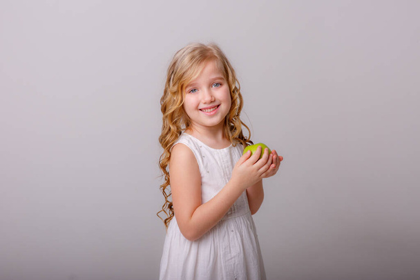 niña con manzana posando sobre fondo gris - Foto, imagen
