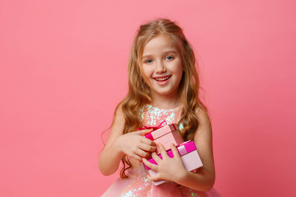 маленькая девочка с подарками в руках улыбается на розовом фоне. - Фото, изображение
