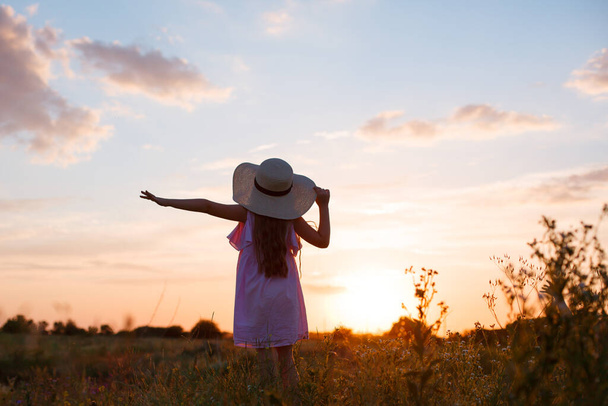 mała dziewczynka w kapeluszu pozowanie na polu o zachodzie słońca - Zdjęcie, obraz