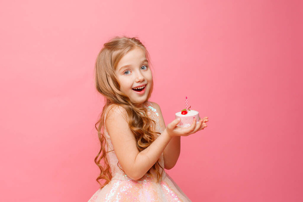 schattig klein meisje poseren tegen roze achtergrond met verjaardag cupcake - Foto, afbeelding