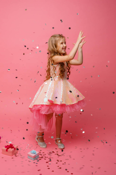 fröhliches kleines Mädchen fängt Konfetti auf rosa Hintergrund, Urlaubskonzept - Foto, Bild