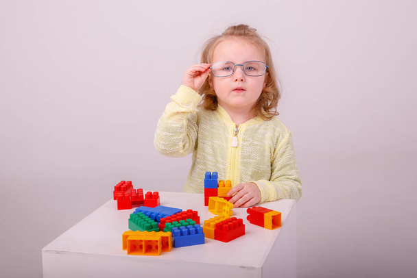 little cute blonde girl playing in a constructor on a white background. Concept of preschool education - Фото, изображение