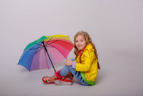χαριτωμένο κοριτσάκι ποζάρουν στο στούντιο σε κίτρινο αδιάβροχο με ομπρέλα ουράνιο τόξο  - Φωτογραφία, εικόνα