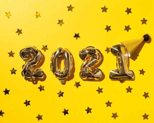 2021 золотые воздушные шары с приветственной шапкой и конфетти из золотых звезд на бумажном фоне. Рождественская или новогодняя праздничная концепция. Вид сверху и плоская кладка. - Фото, изображение