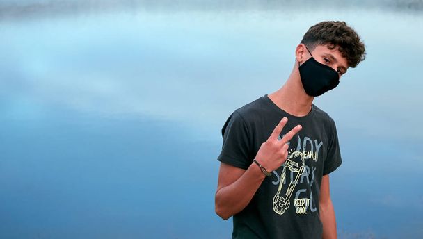 A young Caucasian man wearing a black mask and posing in front of a blue lake - Φωτογραφία, εικόνα