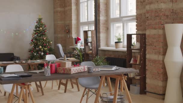 PAN záběr interiéru prázdné startup firemní kanceláře zdobené na Vánoce. Zabalené dárky jsou na stole. Vánoční strom a blikající víla světla v pozadí - Záběry, video