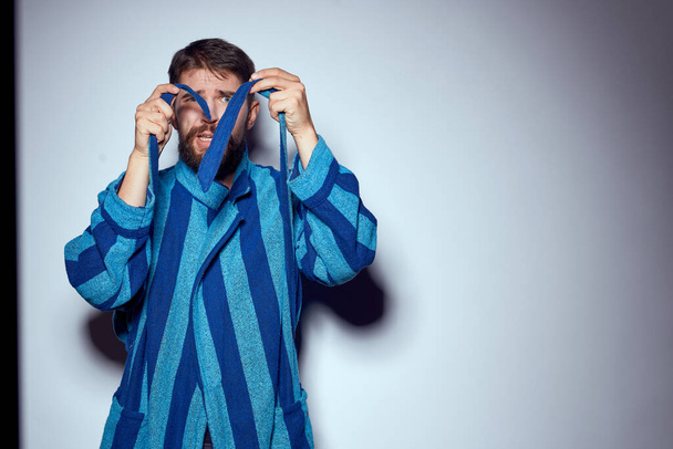 emotional man in a blue striped robe with a belt on a light background cropped view close-up - Photo, image