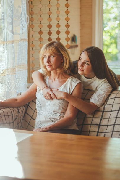 Loving adult 20s daughter hug elderly mother from behind while mom sitting on couch people posing looking at camera smiling feels happy, concept of multi generational family, relative devoted person - Photo, Image