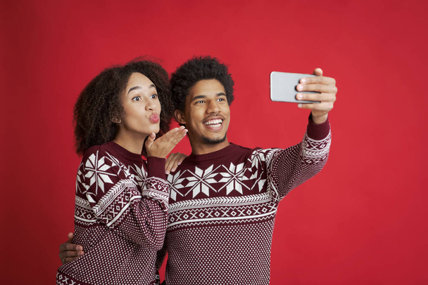 Селфи влюблённой пары. Счастливый африканский американец держит смартфон, леди дует поцелуй или сделать видео-звонок - Фото, изображение