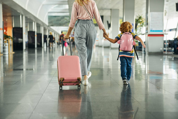 Woman guiding a kid through an airport hall - Foto, afbeelding