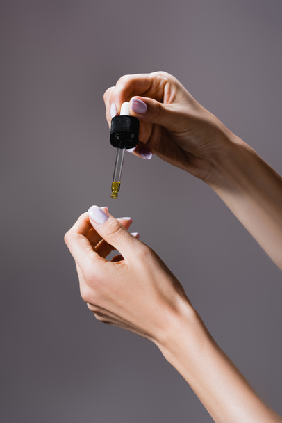 cropped view of woman applying oil from pipette on fingernails isolated on grey - Fotó, kép