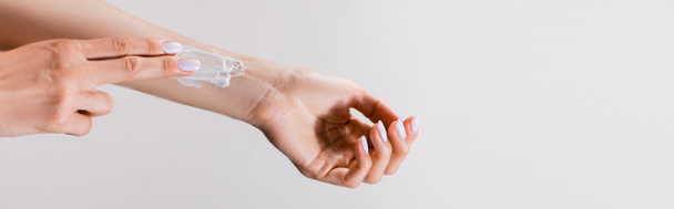 vista ritagliata della donna con crema per le mani sul braccio isolato su grigio, banner - Foto, immagini