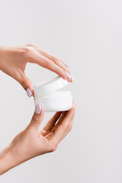 cropped view of woman opening container of hand cream isolated on grey - Fotografie, Obrázek