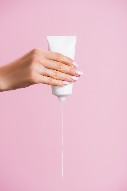 bijgesneden weergave van vrouw knijpen hand crème geïsoleerd op roze - Foto, afbeelding