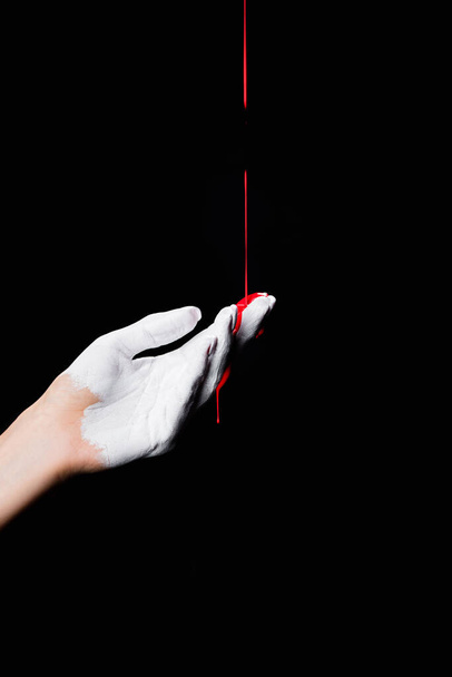 częściowy widok białej malowanej dłoni z czerwoną farbą kapiącą izolowaną na czarno - Zdjęcie, obraz