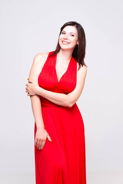 Happy woman in red dress with deep neckline in studio on gray background, - Zdjęcie, obraz