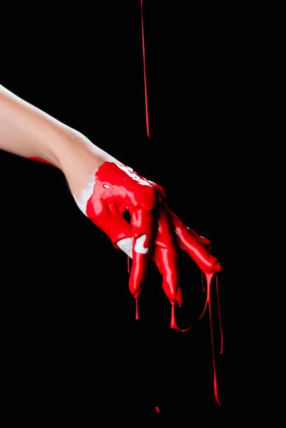 gedeeltelijke weergave van geschilderde hand met rode druppelende verf geïsoleerd op zwart - Foto, afbeelding