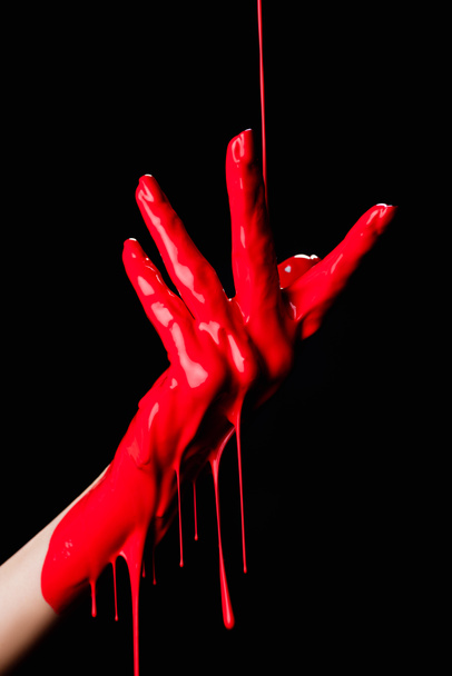 vista parcial de la mano pintada con pintura de goteo rojo aislada en negro - Foto, Imagen
