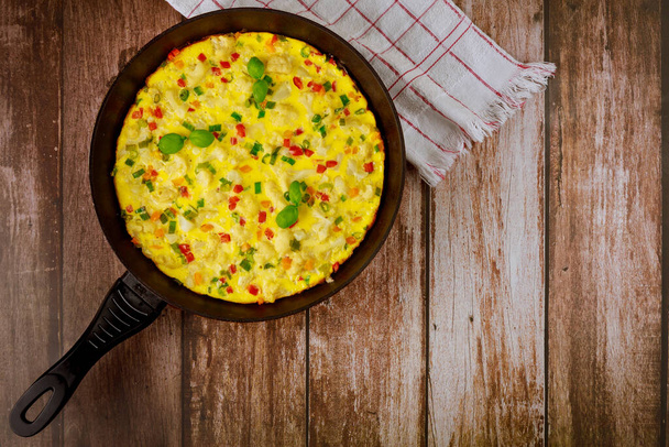Zelfgemaakte omelet met groenten in pan op houten ondergrond. Gezond voedselconcept. - Foto, afbeelding