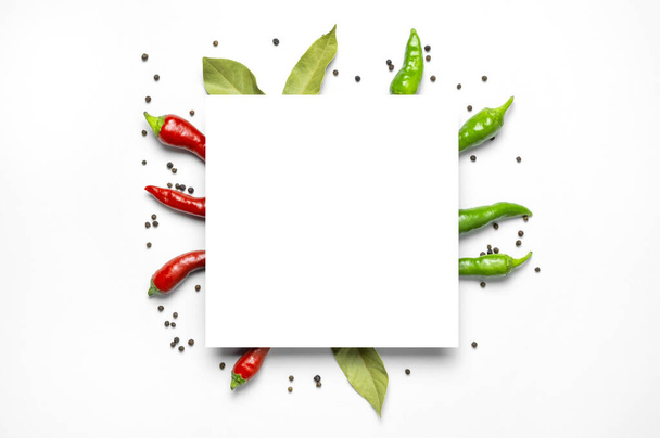 Creative food layout. Hot red and green fresh chili peppers Bay leaf dry black peppercorns, white blank sheet of paper on white background flat lay top view. Spicy spices for cooking, cayenne pepper. - Foto, imagen